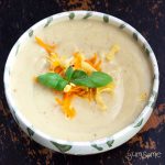 Overhead view of a bowl of creamy vegan cauliflower cheese soup on a black table.