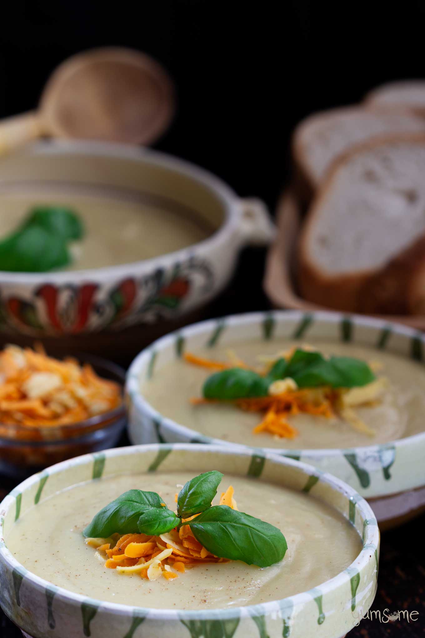 Several bowls of vegan cauliflower cheese soup, garnished with grated cheese and basil, on a black table.