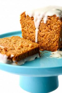 Sliced pumpkin bread on a blue cake stand, topped with white frosting.