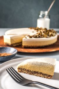 A slice of vegan pumpkin cheesecake on a white plate, with a fork.