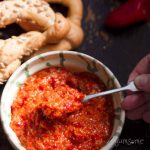 A spoonful of zacusca being taken from a bowl.