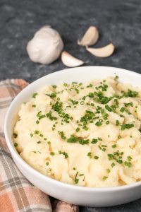 A bowl of garlic mashed potatoes garnished with chopped herbs.