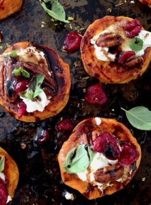 Several slices of roast sweet potato with various toppings on them, on a black background.