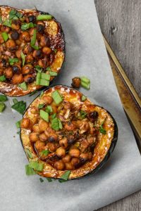 A baking tray lined with greaseproof paper, upon which are two halves of vegan hoisin-glazed stuffed acorn squash.
