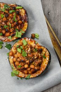 A baking tray lined with greaseproof paper, upon which are two halves of vegan hoisin-glazed stuffed acorn squash.