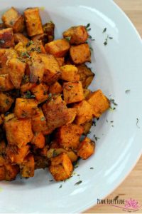 A white dish filled with cubes of roast sweet potato, garnished with chopped herbs.