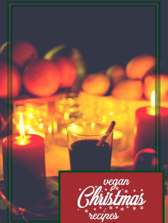 A glass of mulled wine with a cinnamon stick, surrounded by candles and Christmas fruits.