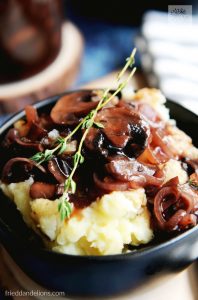 A pile of mashed potatoes, slathered in vegan red wine and mushroom gravy.