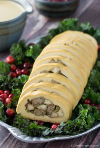A stuffed vegan turkey roll on a bed of greens, with some cranberries scattered around.