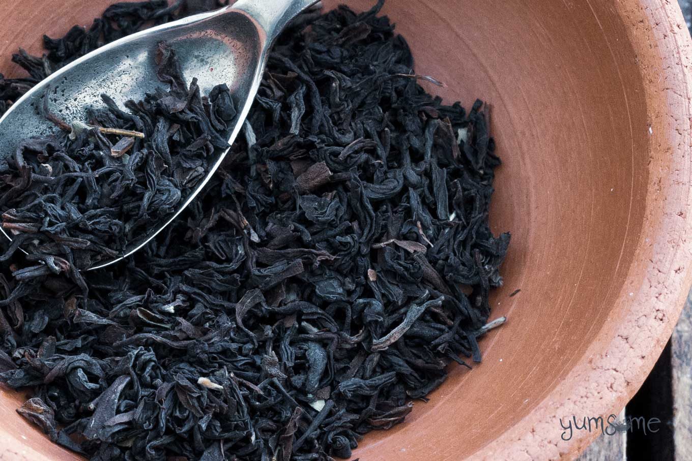 Loose leaf Assam tea in a clay bowl with a silver spoon.