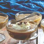 Vegan butterscotch pudding in glass bowls, against a purple and blue background.