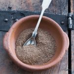 A silver spoon sits in a clay bowl of chai masala.