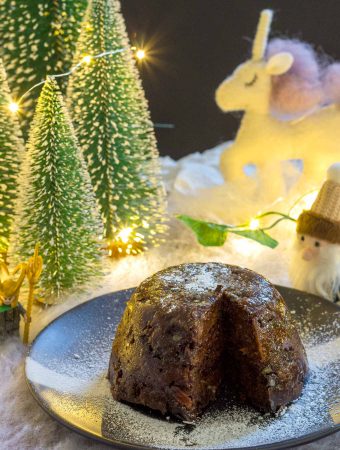 A vegan Christmas pudding, on a black plate, with a slice cut from it.