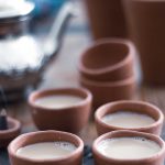 Several small clay cups on a wooden table, containing vegan masala chai.