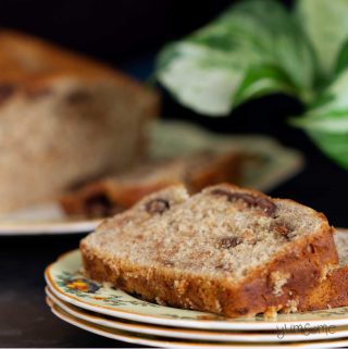 Two slices of chocolate chip banana bread on a stack of plate with a loaf and a green plant.