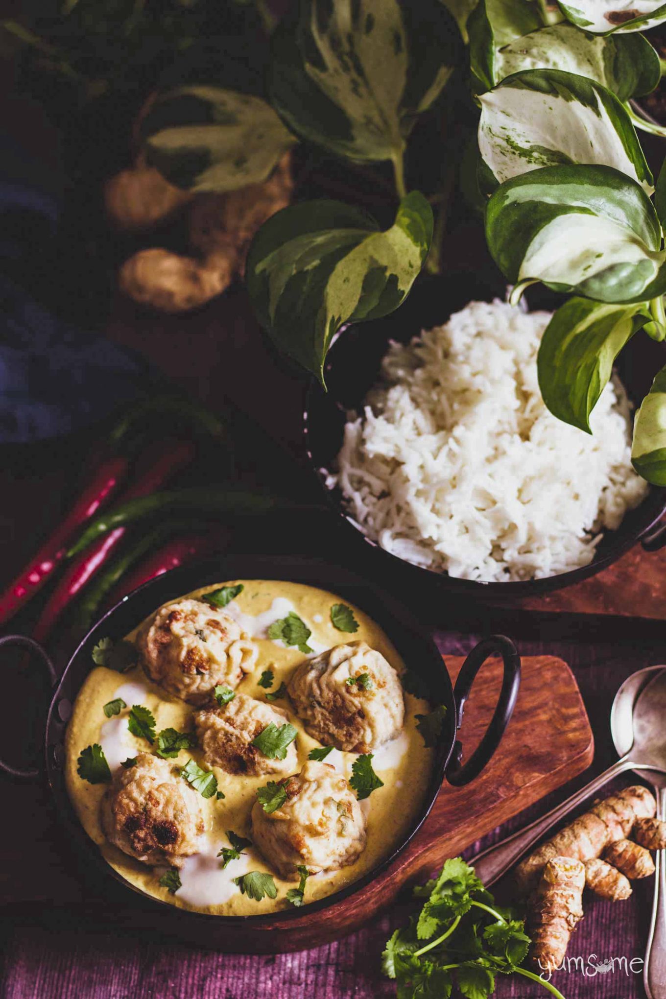 Two bowls of malai kofte and rice on a wooden table.