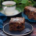 Festive bread pudding on a black plate with a cup of tea in the background.