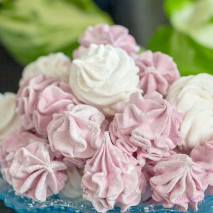 A pile of fluffy pink and white vegan marshmallows on a blue plate, with a green background.