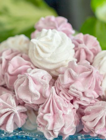 A pile of fluffy pink and white vegan marshmallows on a blue plate, with a green background.